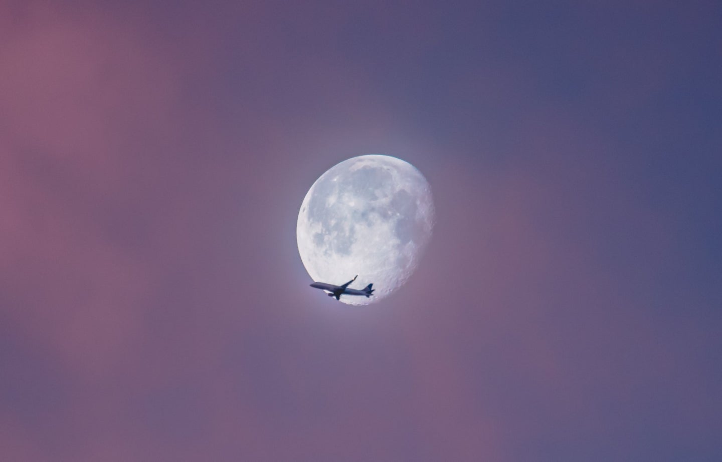 Airplane flying across almost full moon during a long flight