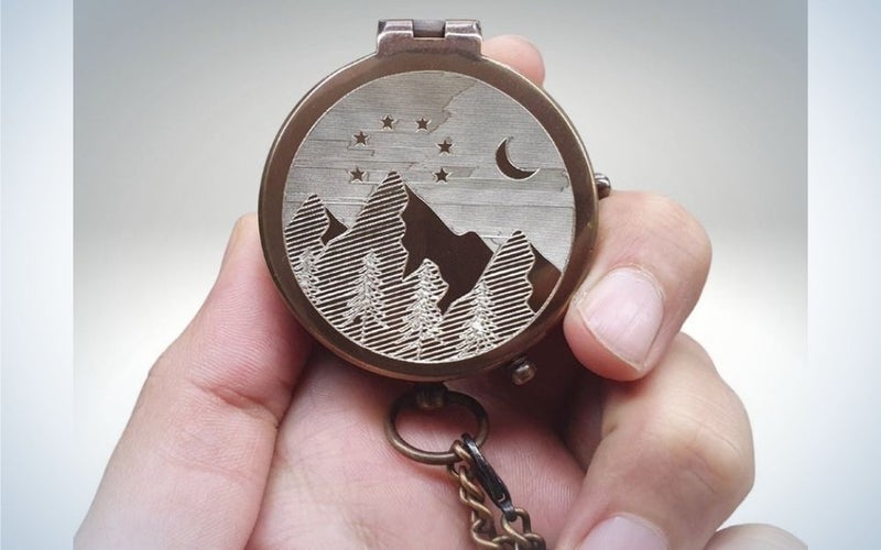 A hand of a person holding into his fingers a picture of a mountain and the moon into a clock shape and form.
